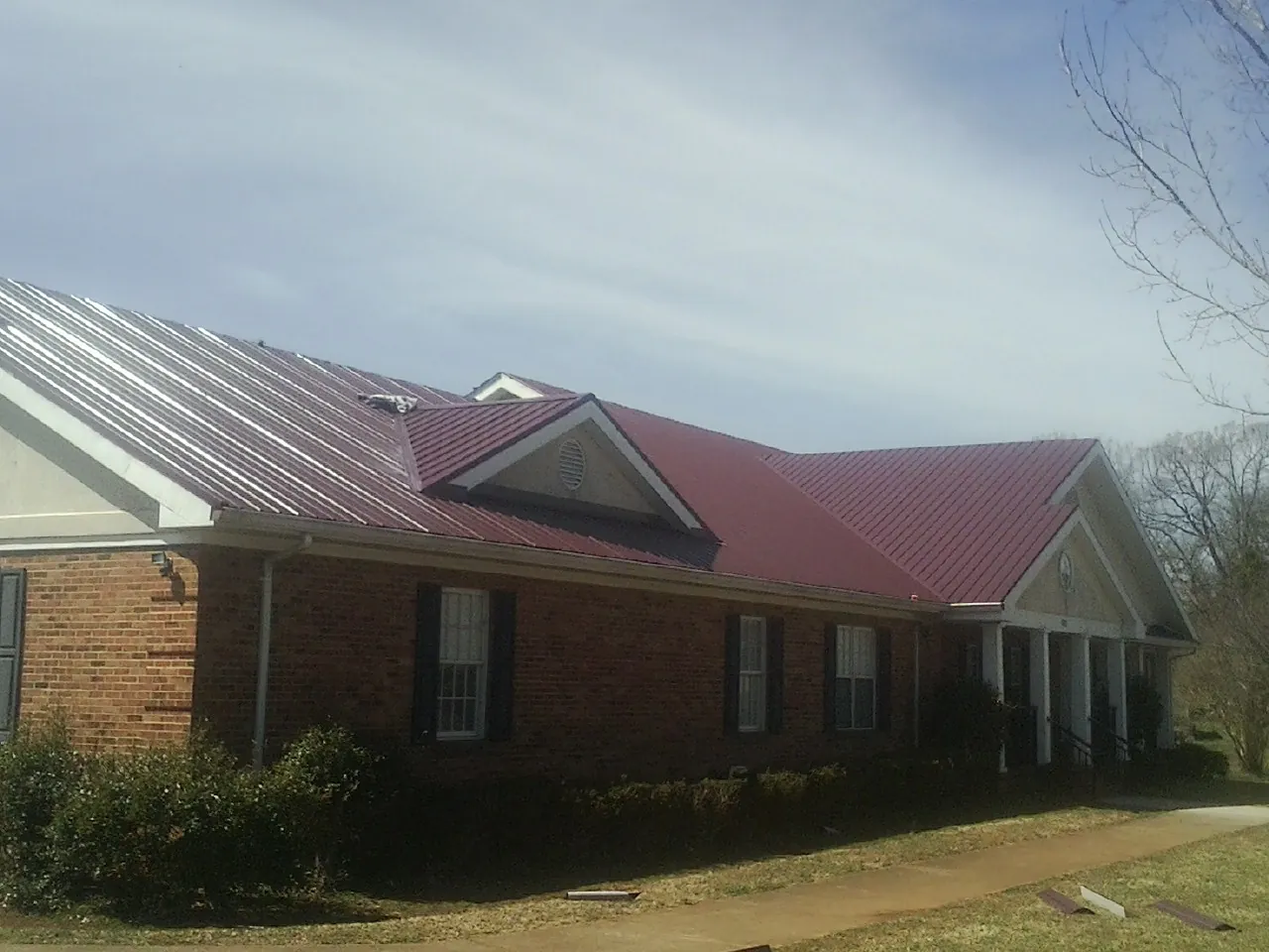 Red metal roof with gabled entries on a long brick building, from a Hail Damage Roof Repair job in Rehoboth Beach