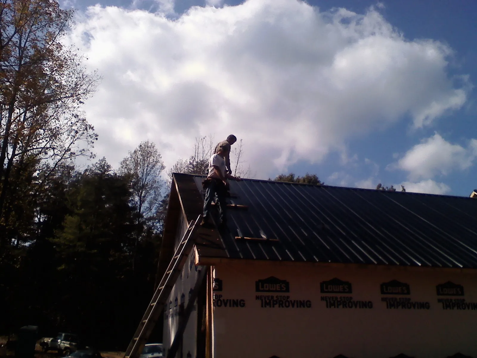 Roofer fastening dark metal panels high against a cloudy sky, from a Roof Inspection job in Rehoboth Beach