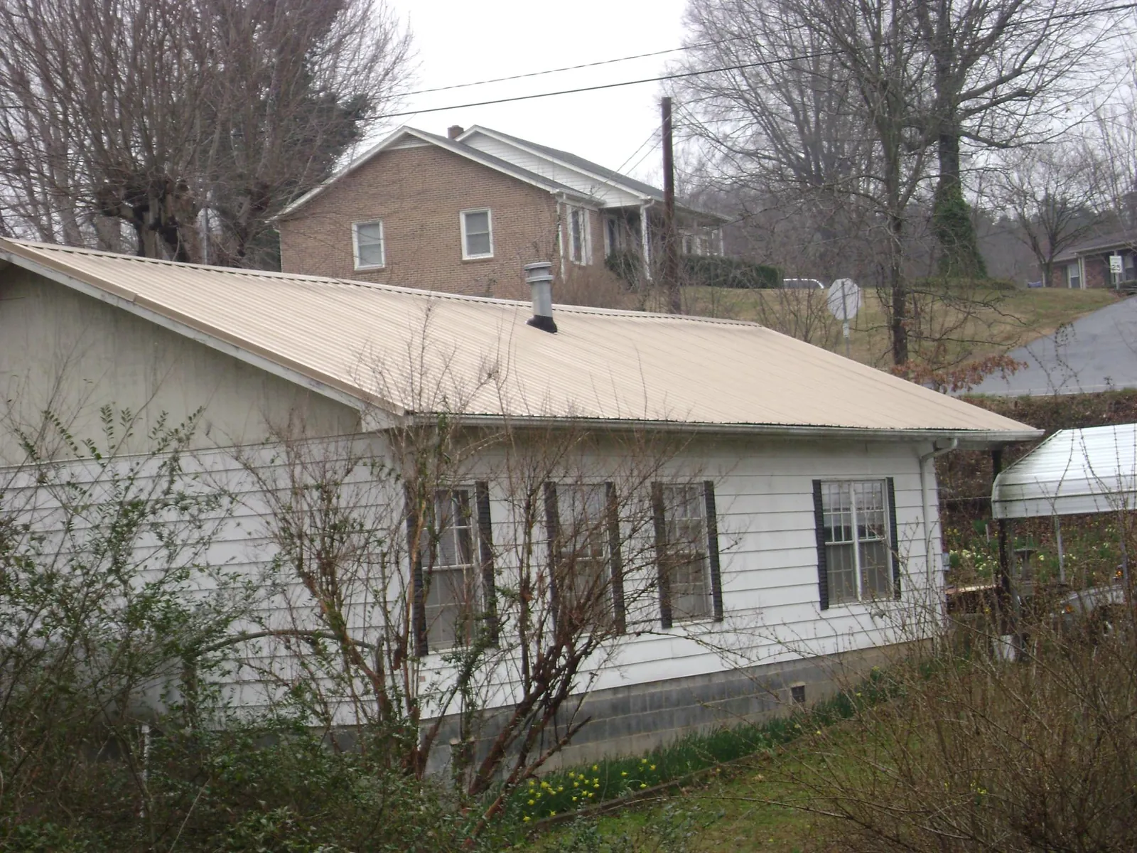 Tan metal roof on a white sided house set into a hillside — Commercial Roofing by Roofing Brothers in Rehoboth Beach